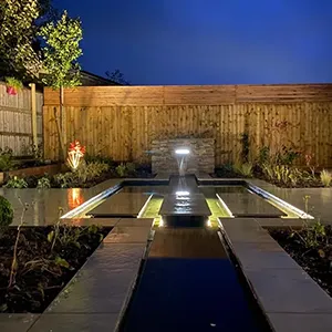 a garden at night with lights on the water